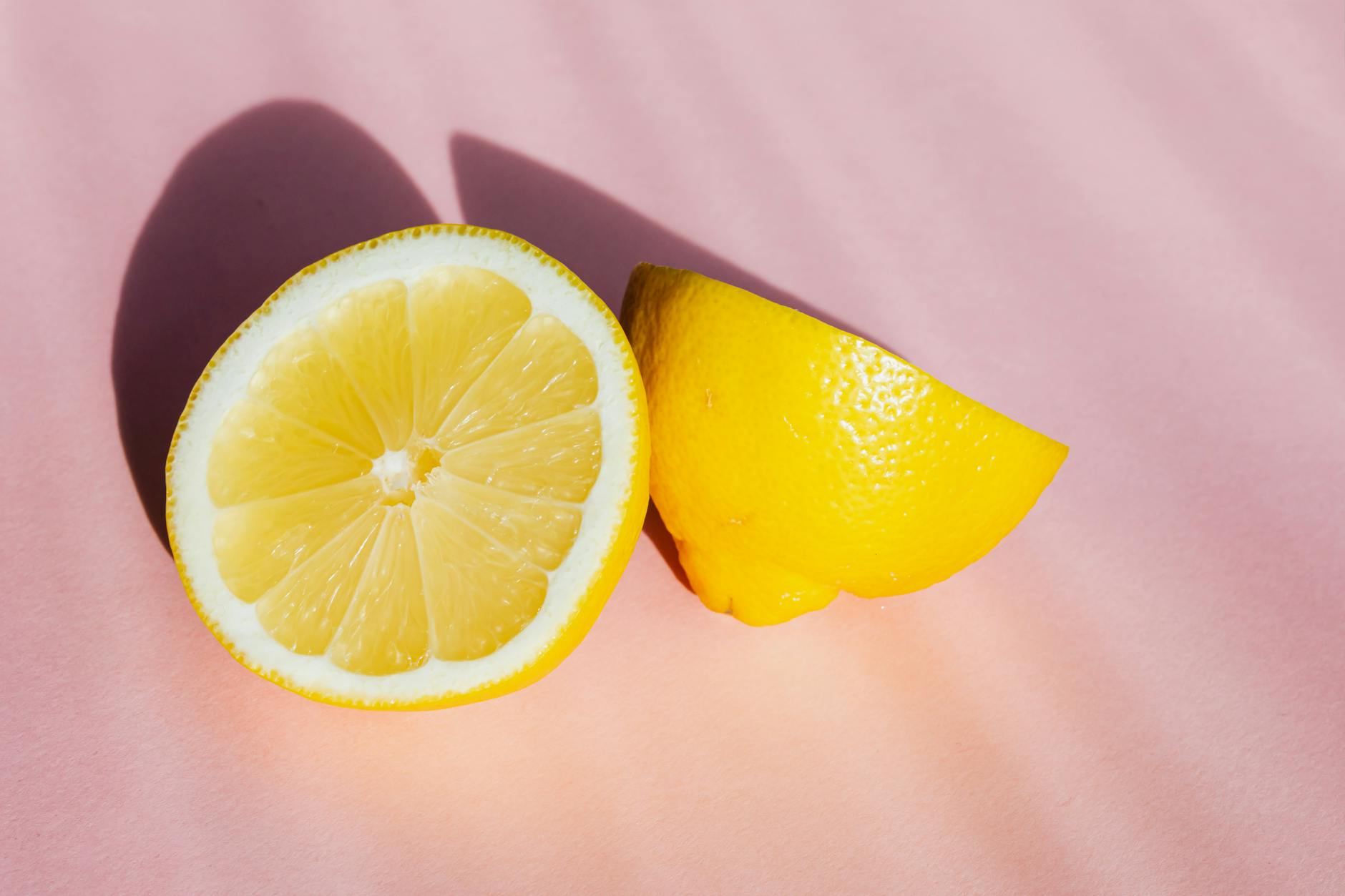 Frische Zitronenhälften auf rosa Hintergrund in Sonnenstrahlen, symbolisiert Frische und Empfindlichkeit