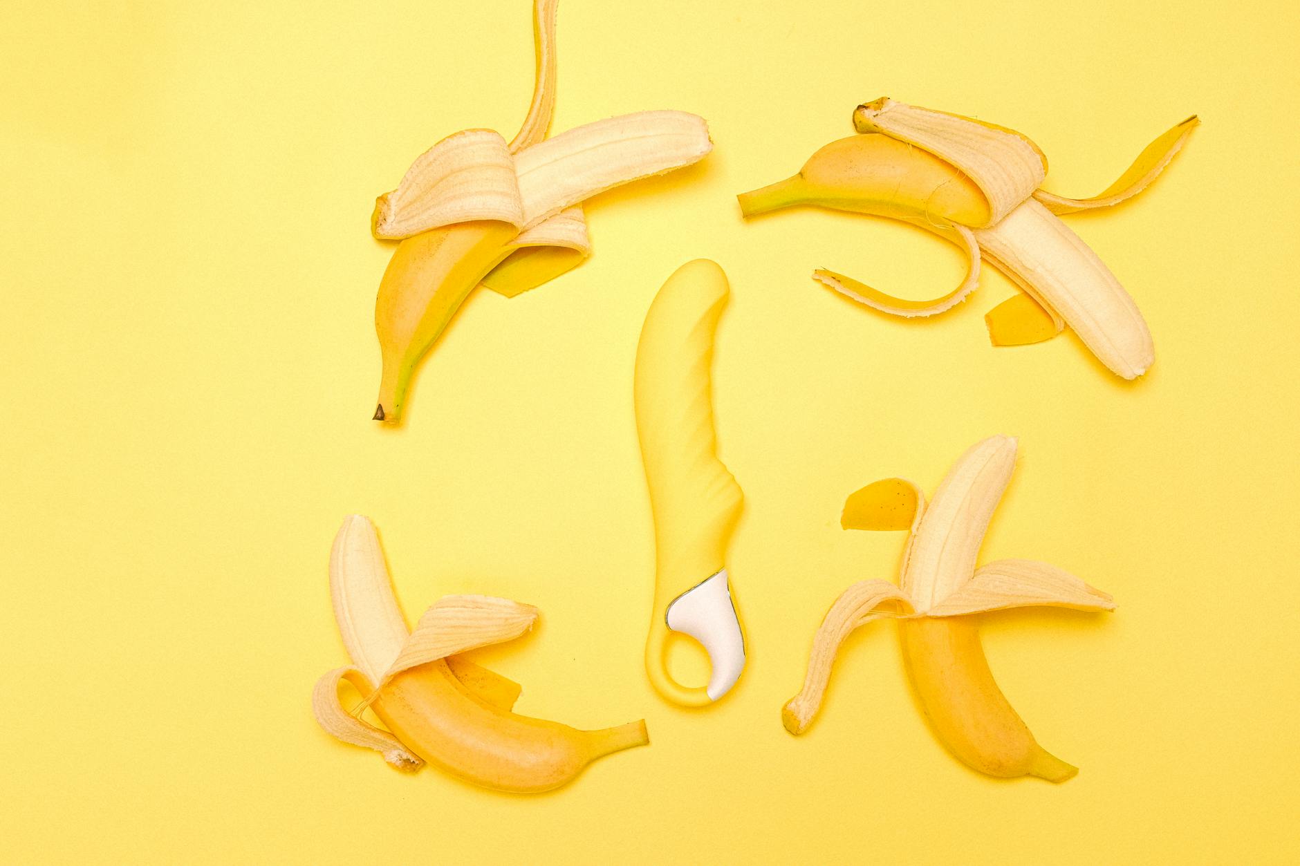 Gelber Silikonvibrator umgeben von geschälten Bananen auf gelbem Hintergrund