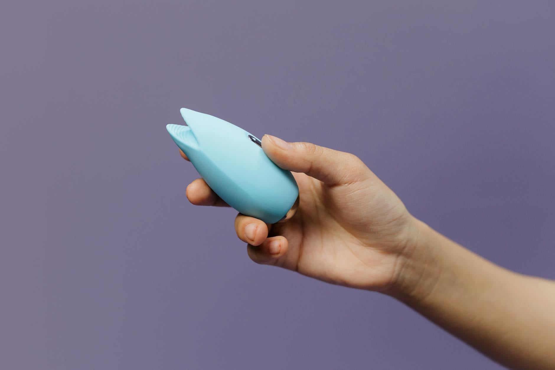 Ein blauer Silikonvibrator in der Hand vor solidem lila Hintergrund, der Selbstliebe und Sexualität fördert