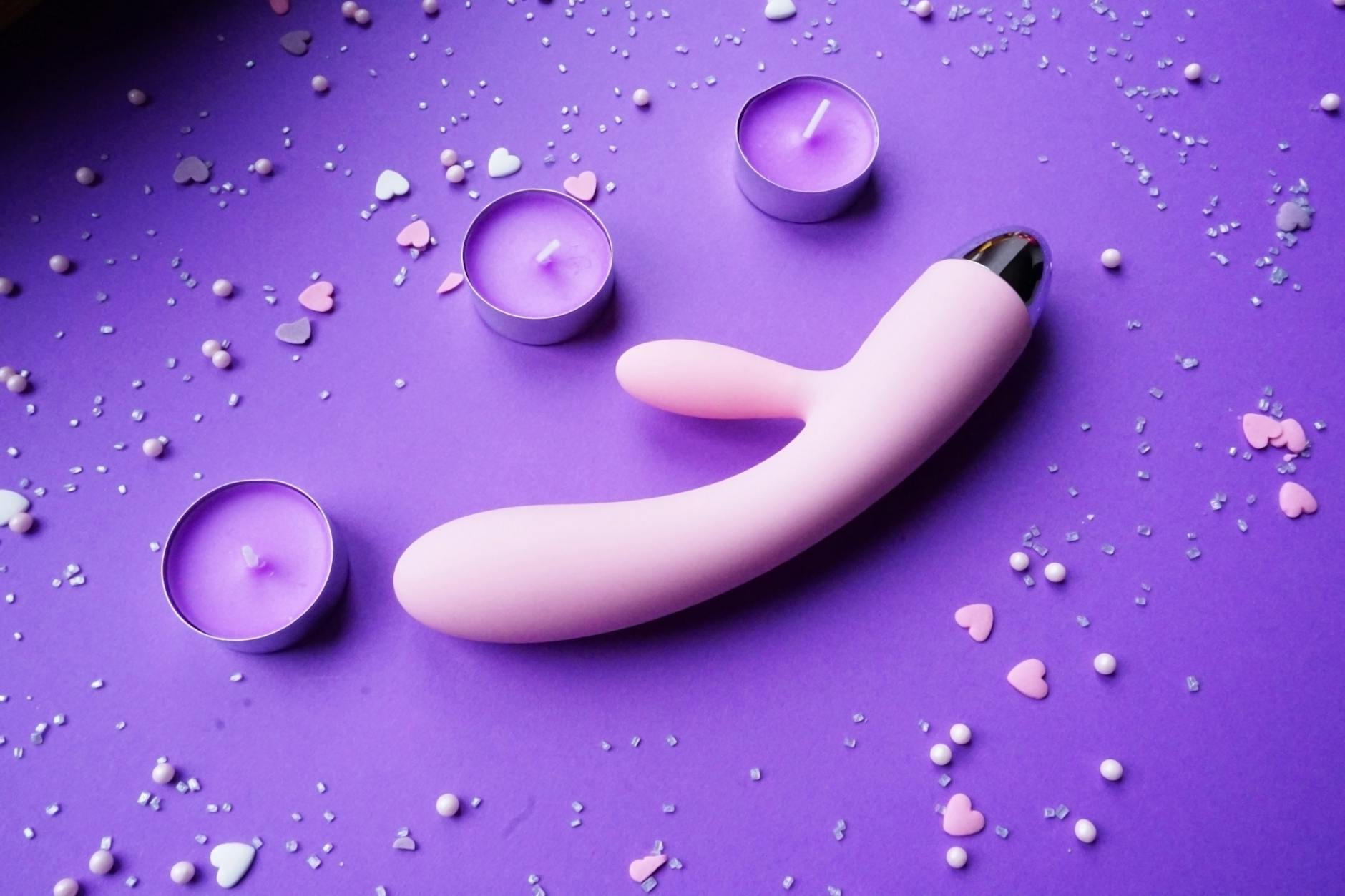 Rosa Vibrator auf violettem Hintergrund mit herzförmigem Konfetti und Kerzen für ein romantisches Ambiente